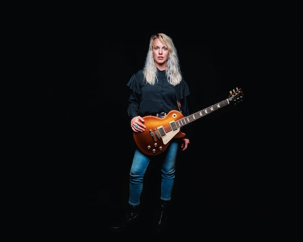 Lauren Calve holding a guitar on black background. Photo by Shane Gardner
