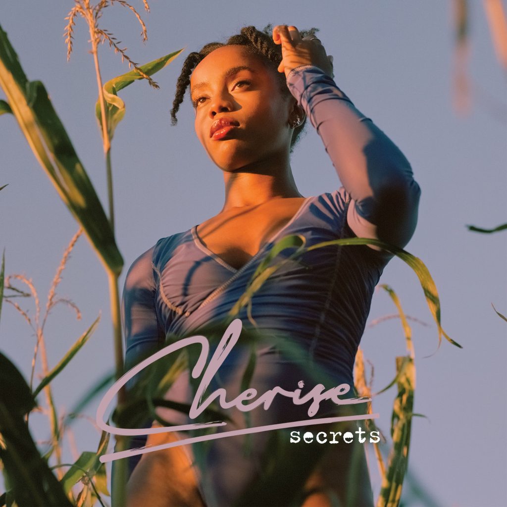 Cherise "Secrets" album art with Cherise standing in a field with the open sky behind her.
