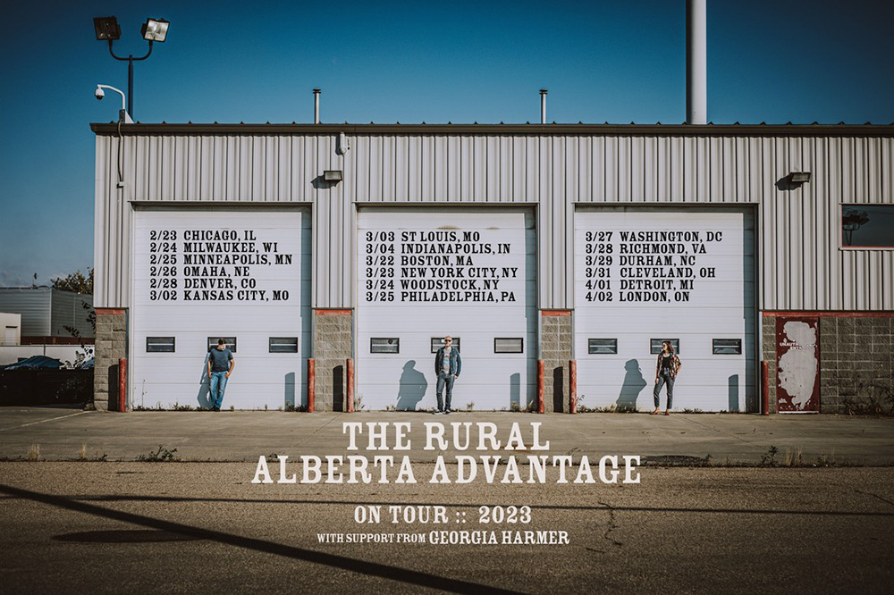 The Rural Alberta Advantage - 2023 Tour Dates - The band lines up in front of the doors of a three car garage
