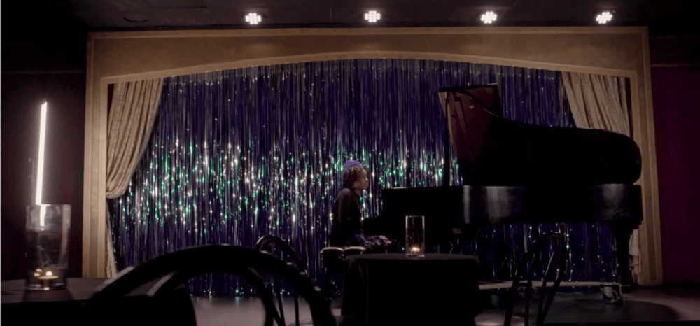 still from "By Your Side" - Cynthia Angelica music video, Cynthia at piano with shimmering blue backdrop