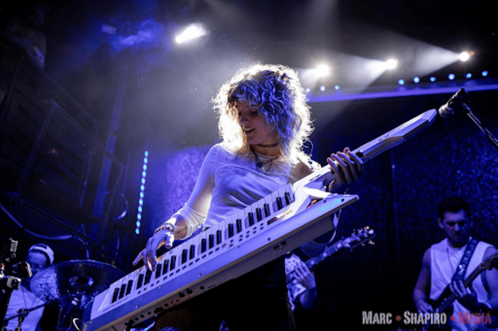 Natalie Brooke playing keytar at a gig, backlit in blue