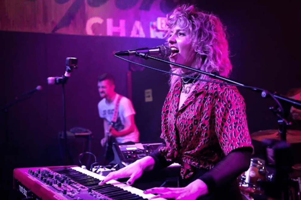 Natalie Brooke playing keyboard at gig, stage lit in pink