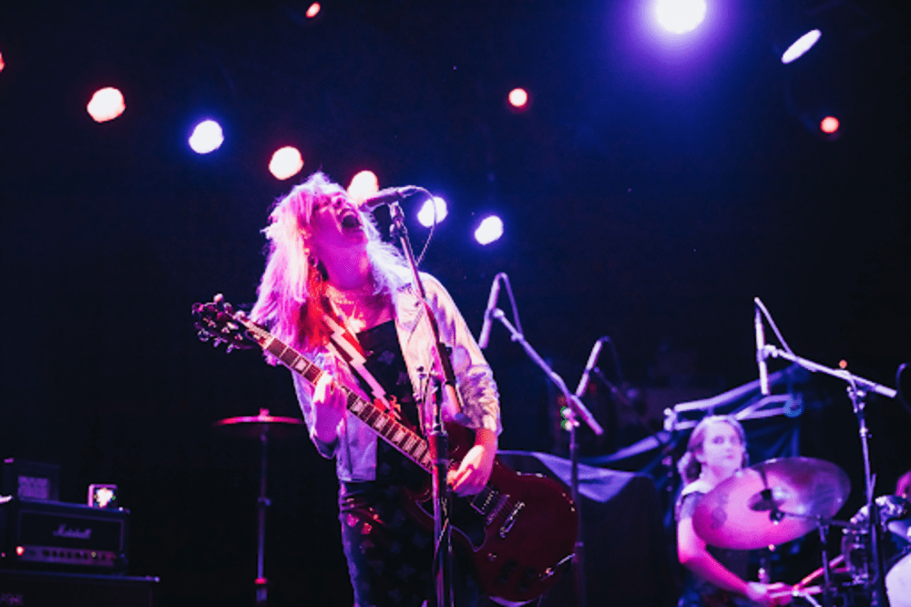 Annie Kuchenmeister of Loki's Folly onstage at a First Avenue show, playing guitar and screaming lyrics with Nissa on the drums by her side