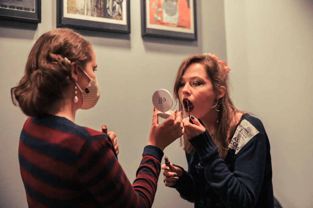 Annie putting on lipstick using a mirror Nissa is holding