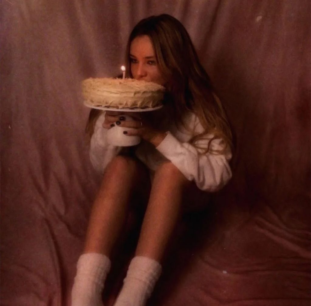Cate Tomlinson - twenty one - album art - Cate sits holding a birthday cake with a solitary lit candle