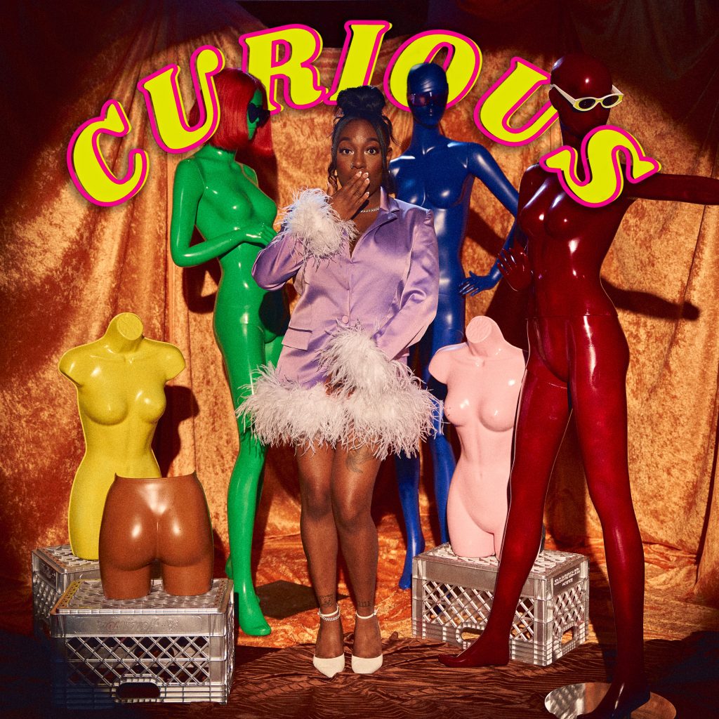 Ainjo - "Curious" album art shows the artist on stage with a number of colorful mannequins.
