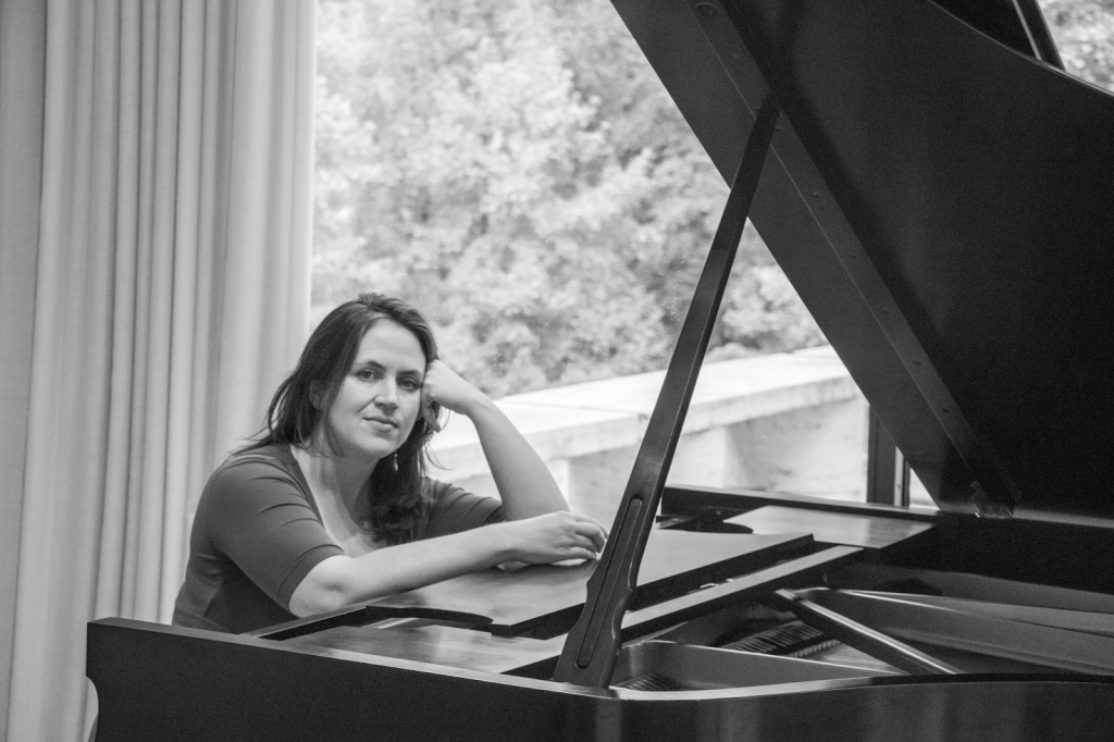 Black and white photo of Amy sitting at/leaning on her piano