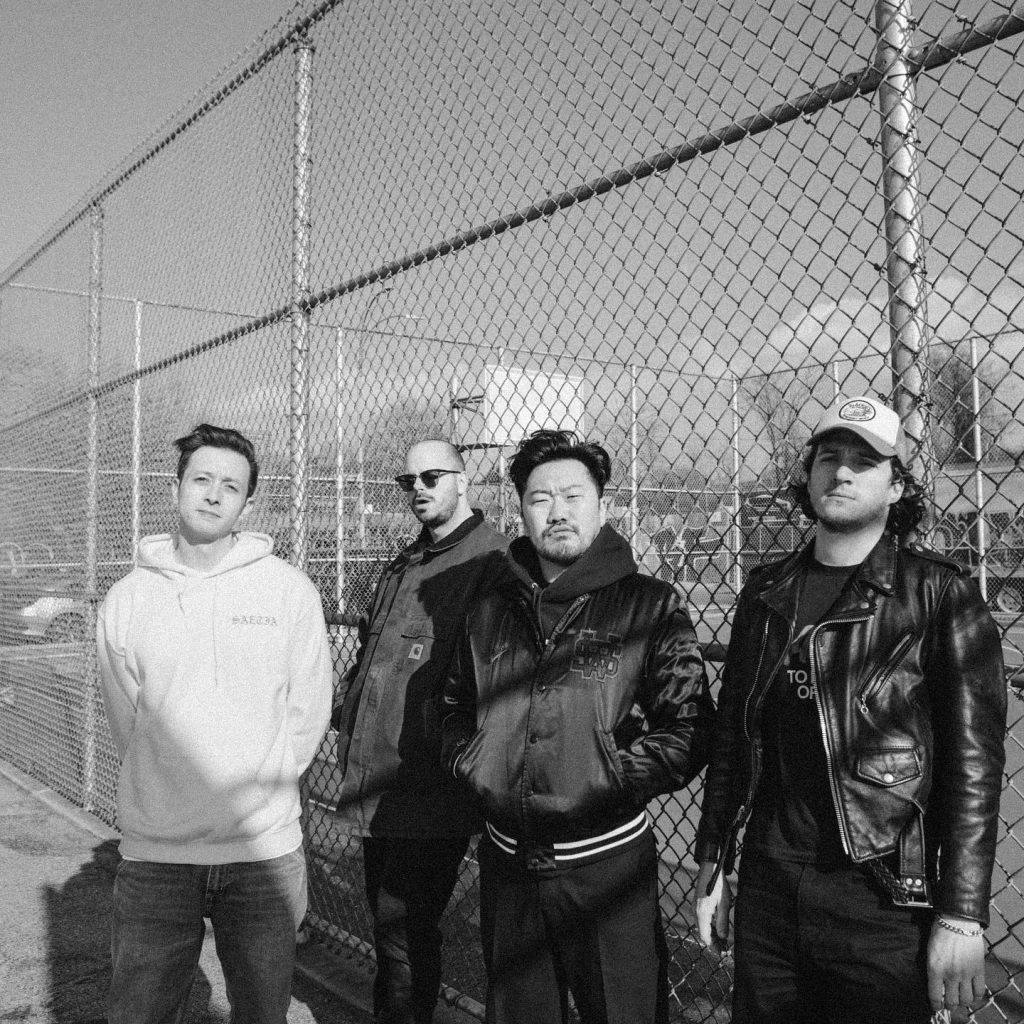 Black and white colored photo of the four band members of Superbloom standing against the metal fence of an outdoor basketball court.