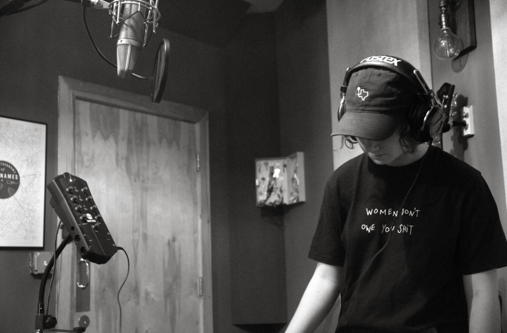 Zola Simone recording in the studio in a shirt that says "Women Don't Owe You Sh*t, black and white photo