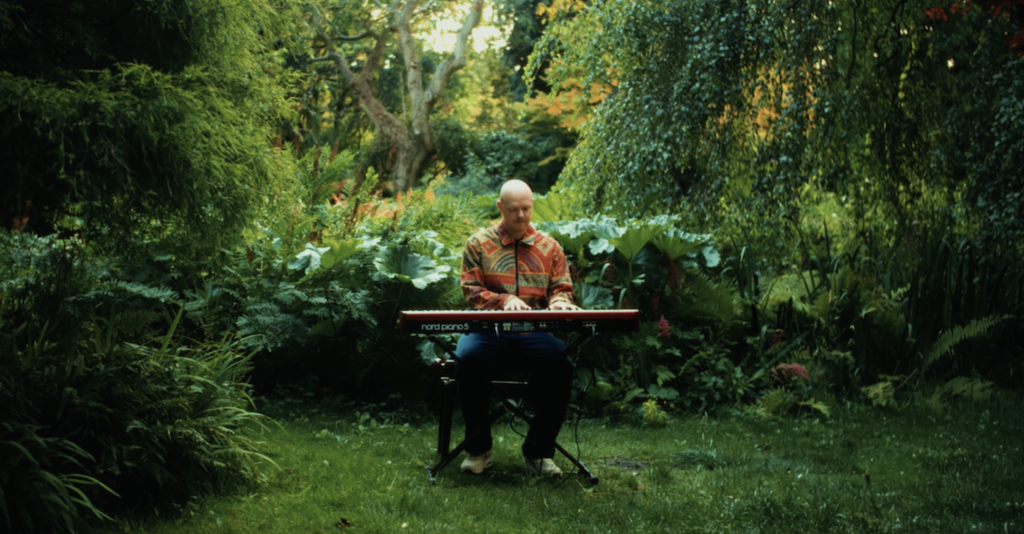 Matt Wilde sitting at his keyboard in the midst of a lush green backdrop