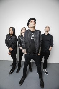 Members of Alternative Rock band Everclear, wearing black while standing on a great concrete floor along a painted white wall.