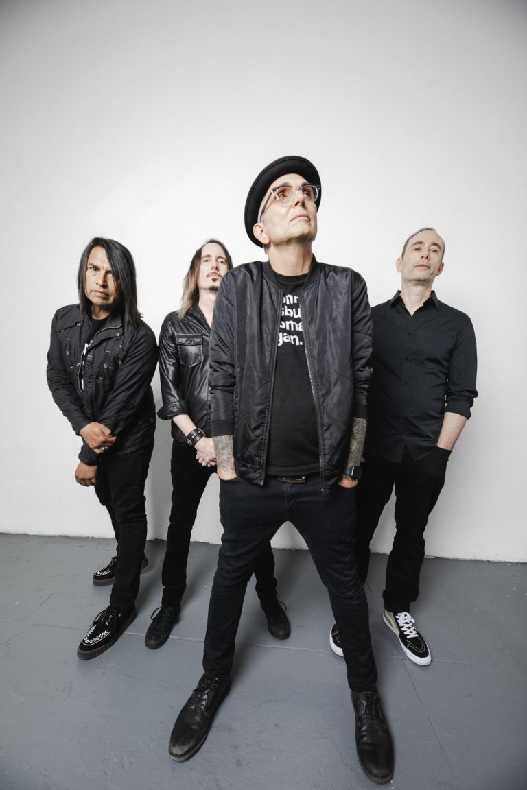 Members of Alternative Rock band Everclear, wearing black while standing on a great concrete floor along a painted white wall.