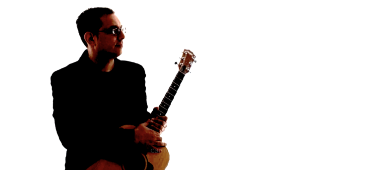 George Katsos holds a guitar while wearing a suit.