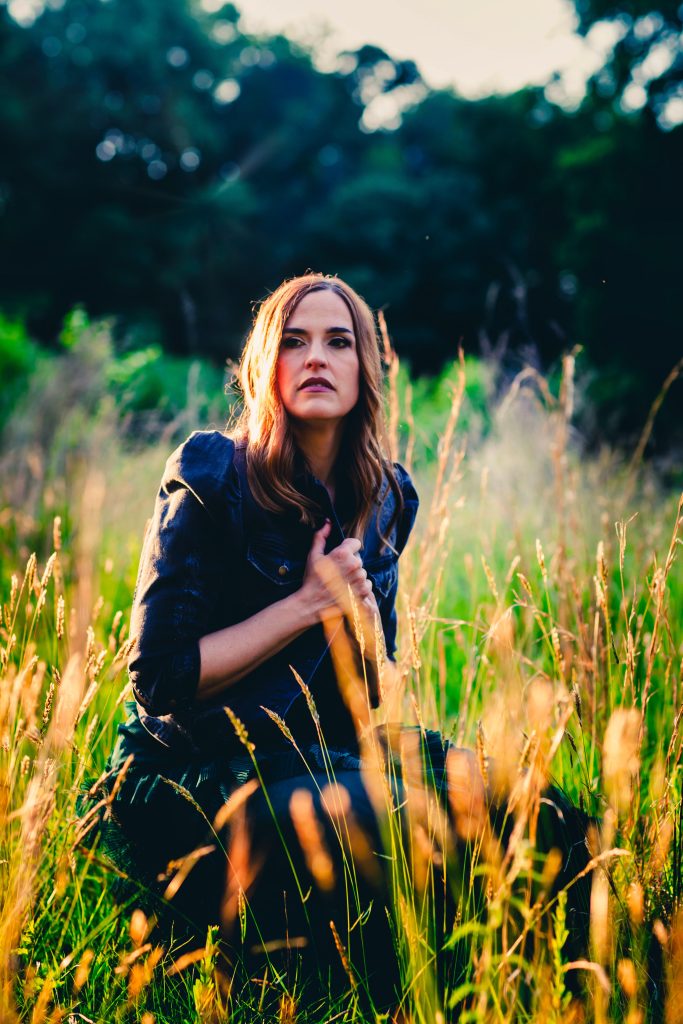 Press photo of Juliet Lloyd sitting in a field while wearing a dress