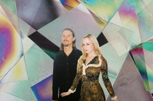 A photograph of Dora Hiller and Aric Bohn from Sneakpeek with a colorful geometric background.