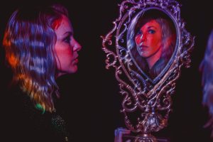 Lauren Calve is looking at her reflection in a red room. The mirror is ornate with twisted metal all around her.