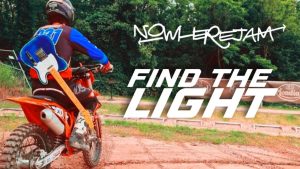 This thumbnail from the "Find The Light" music video shows a motocross rider on a red bike slinging a blue guitar over his shoulder. The band's logo and song title appear on the right hand side of the image.