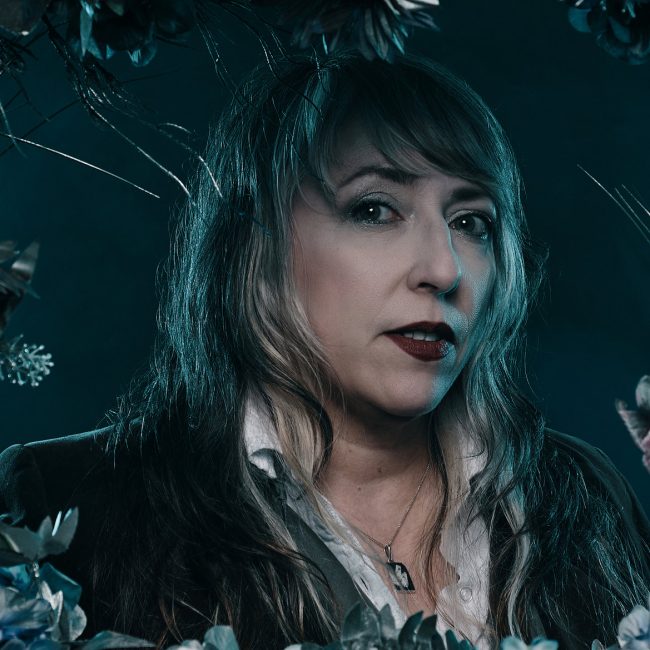 Shirlé Hale is standing in a background with silver foliage around her.