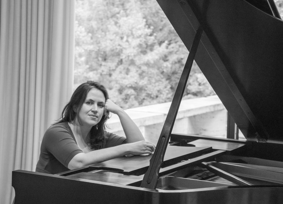 Black and white photo of Amy sitting at/leaning on her piano