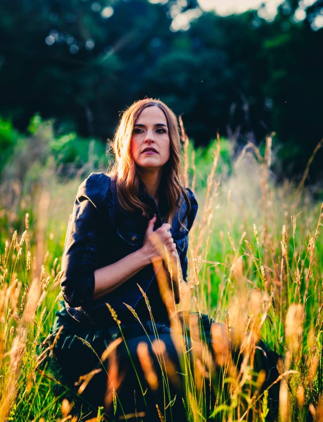 Press photo of Juliet Lloyd sitting in a field while wearing a dress
