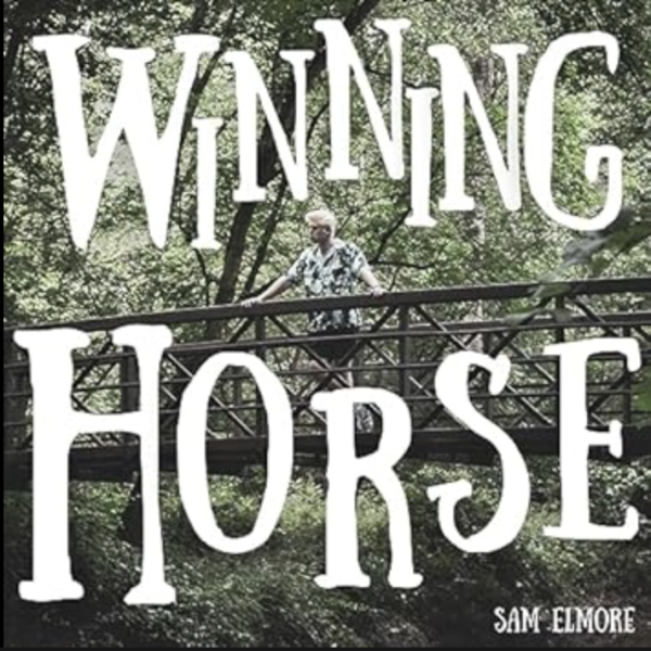 Sam Elmore stands on a wooden bridge surrounded by green foliage.