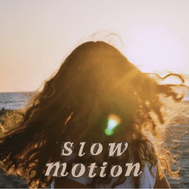 Maggie Cubillos on a beach facing away from the camera and looking into the sky, with 'Slow Motion' written in peach text on the bottom of the image.